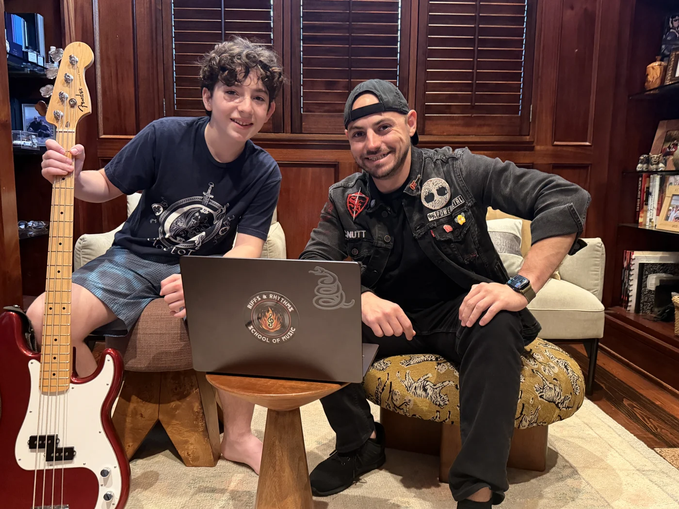Mr. Garrett and a student seated beside a red bass guitar and a laptop with the school logo